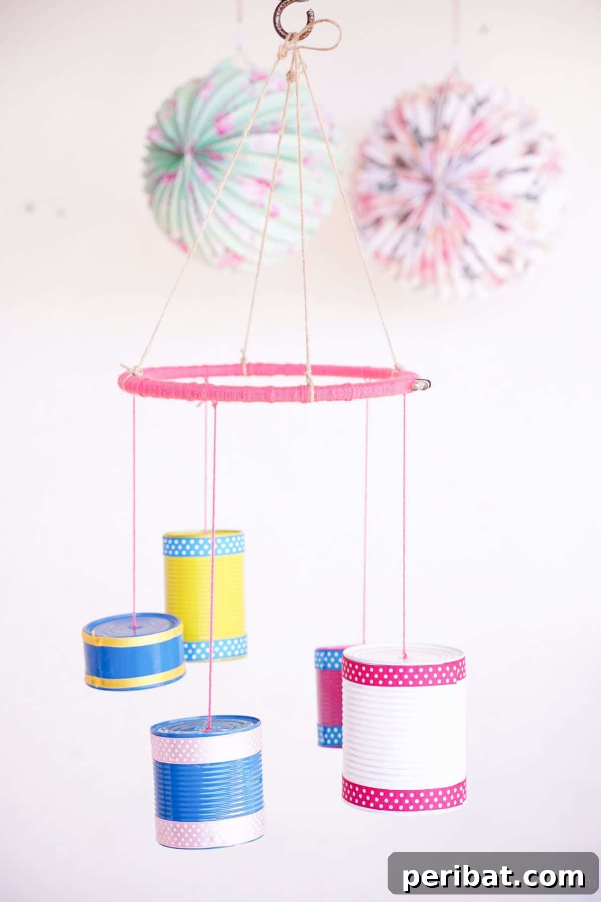Transform Tin Cans into Melodious Wind Chimes 5 A beautifully decorated tin can wind chime with a vibrant pink base, artfully hanging against a clean white wall, showcasing its craftsmanship