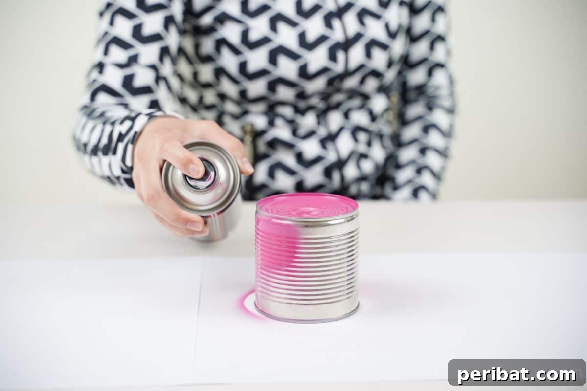 Transform Tin Cans into Melodious Wind Chimes 9 A skilled hand expertly applying vibrant pink spray paint to a tin can, demonstrating the painting process