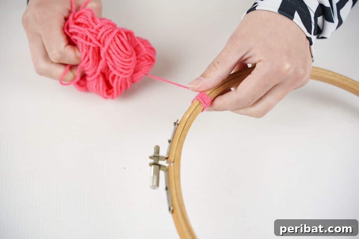 Transform Tin Cans into Melodious Wind Chimes 10 A pair of hands carefully and methodically wrapping vibrant pink yarn around an embroidery hoop, showcasing the beginning of the wrapping process