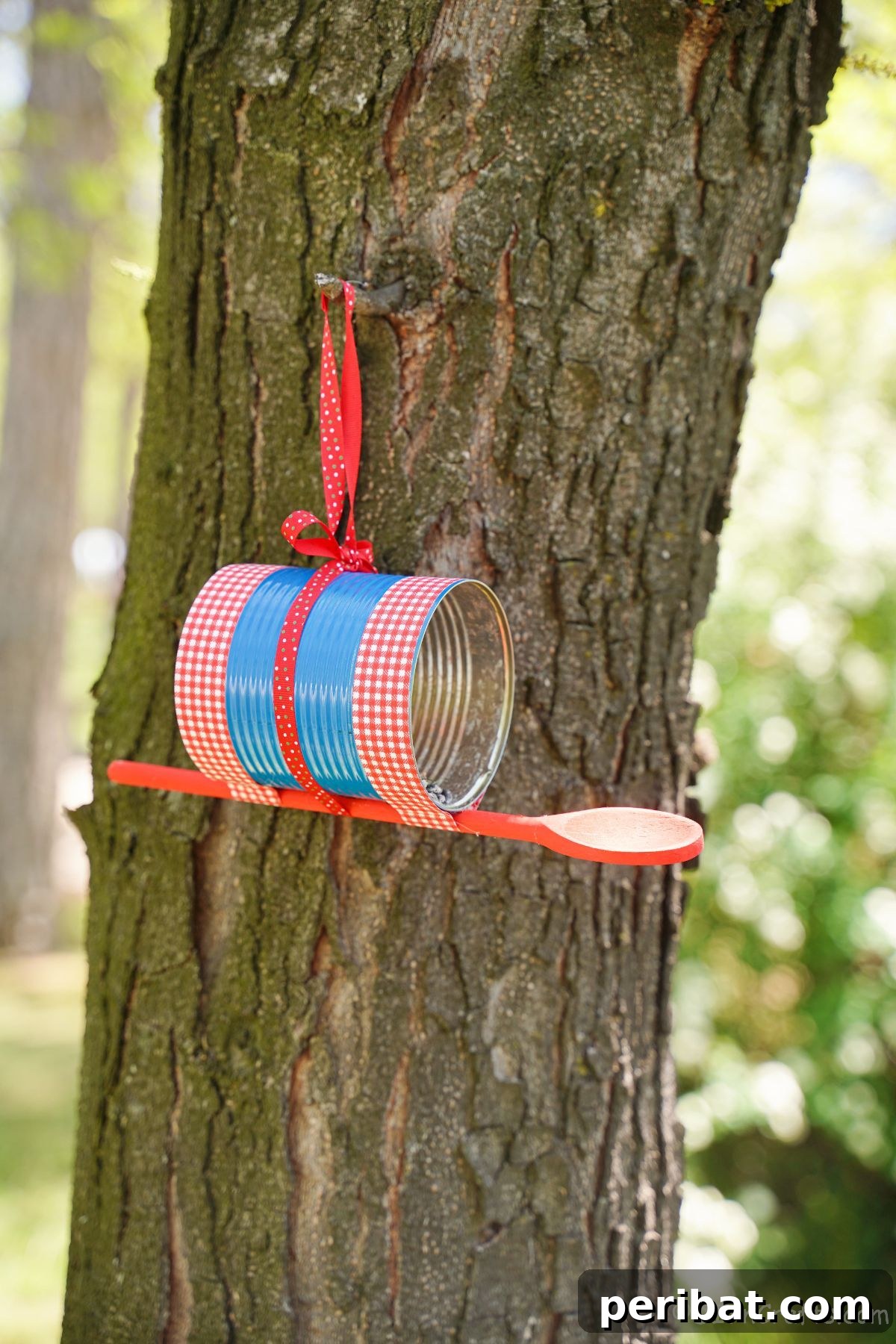Sweet DIY Tin Can Bird Feeder 2 A beautifully decorated tin can bird feeder in blue and red, hanging gracefully on a tree branch, inviting feathered friends.