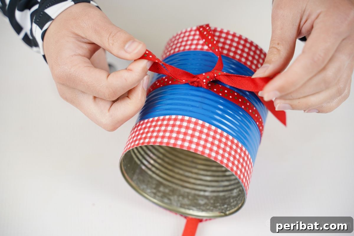 Sweet DIY Tin Can Bird Feeder 12 A hand skillfully ties a red polka dot ribbon into a charming bow around the center of the tin can bird feeder, adding a final decorative touch.