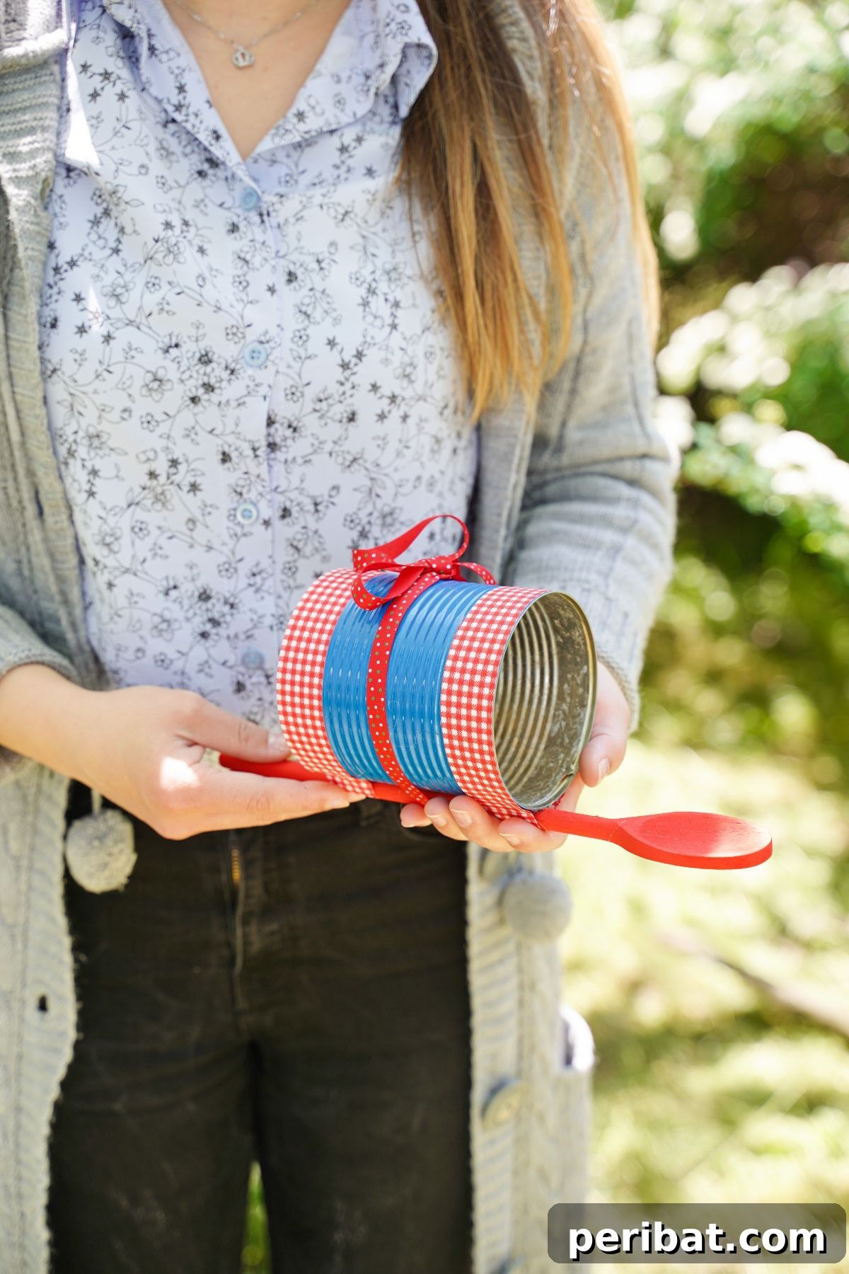 Sweet DIY Tin Can Bird Feeder 5 A woman in black jeans gently holds a newly crafted blue and red tin can bird feeder, showcasing its charming design.
