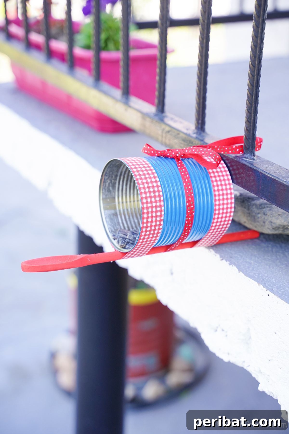 Sweet DIY Tin Can Bird Feeder 6 A charming tin can bird feeder, painted and decorated, rests securely on the edge of a porch railing, ready for birds.