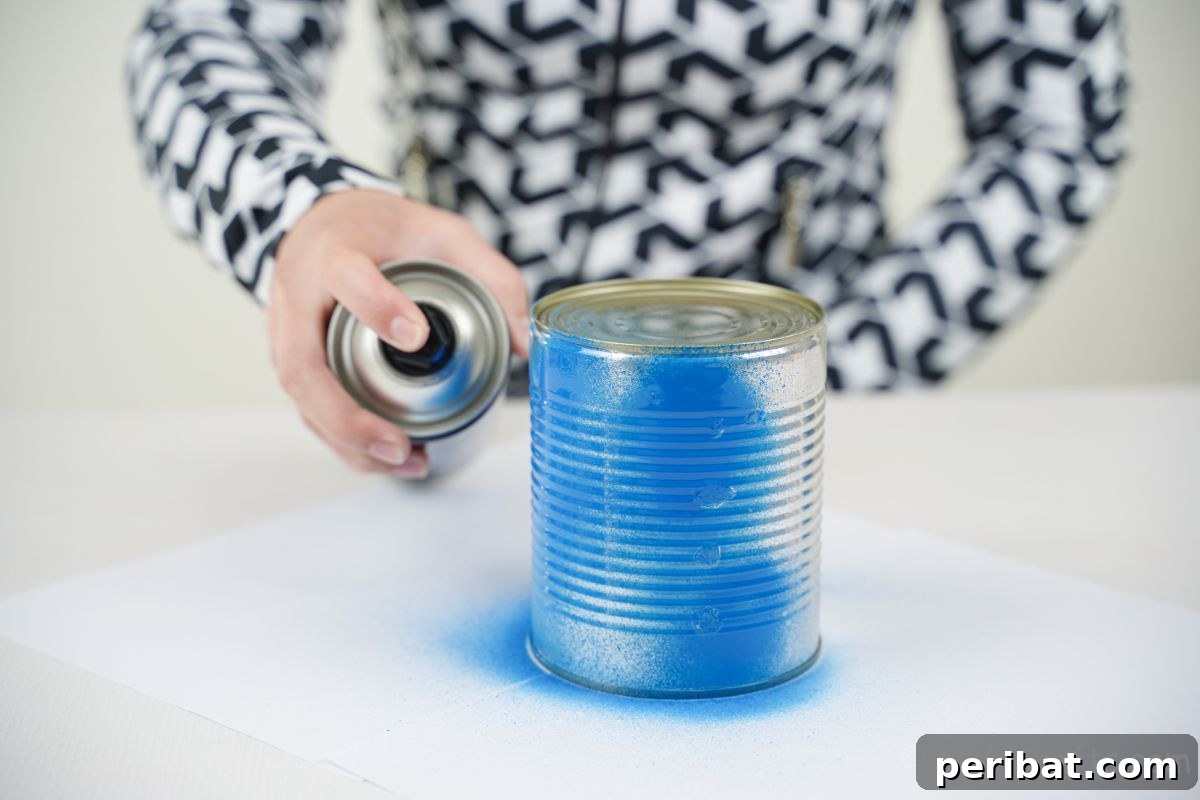 Sweet DIY Tin Can Bird Feeder 8 A person in black and white attire carefully sprays a tin can with blue paint, initiating the transformation into a bird feeder.