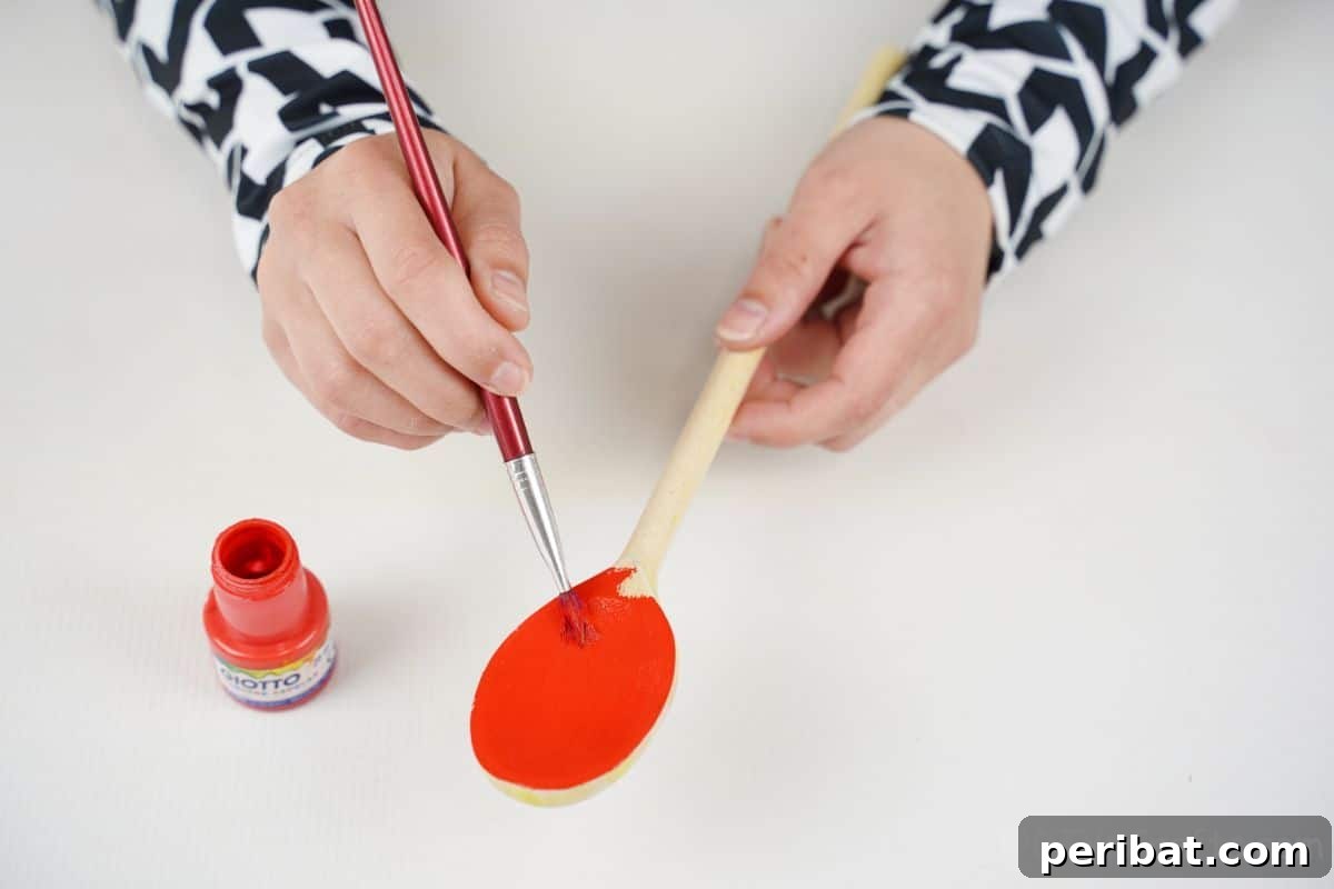 Sweet DIY Tin Can Bird Feeder 9 A hand expertly applies red paint to a wooden spoon, preparing it to become a vibrant perch for the bird feeder.