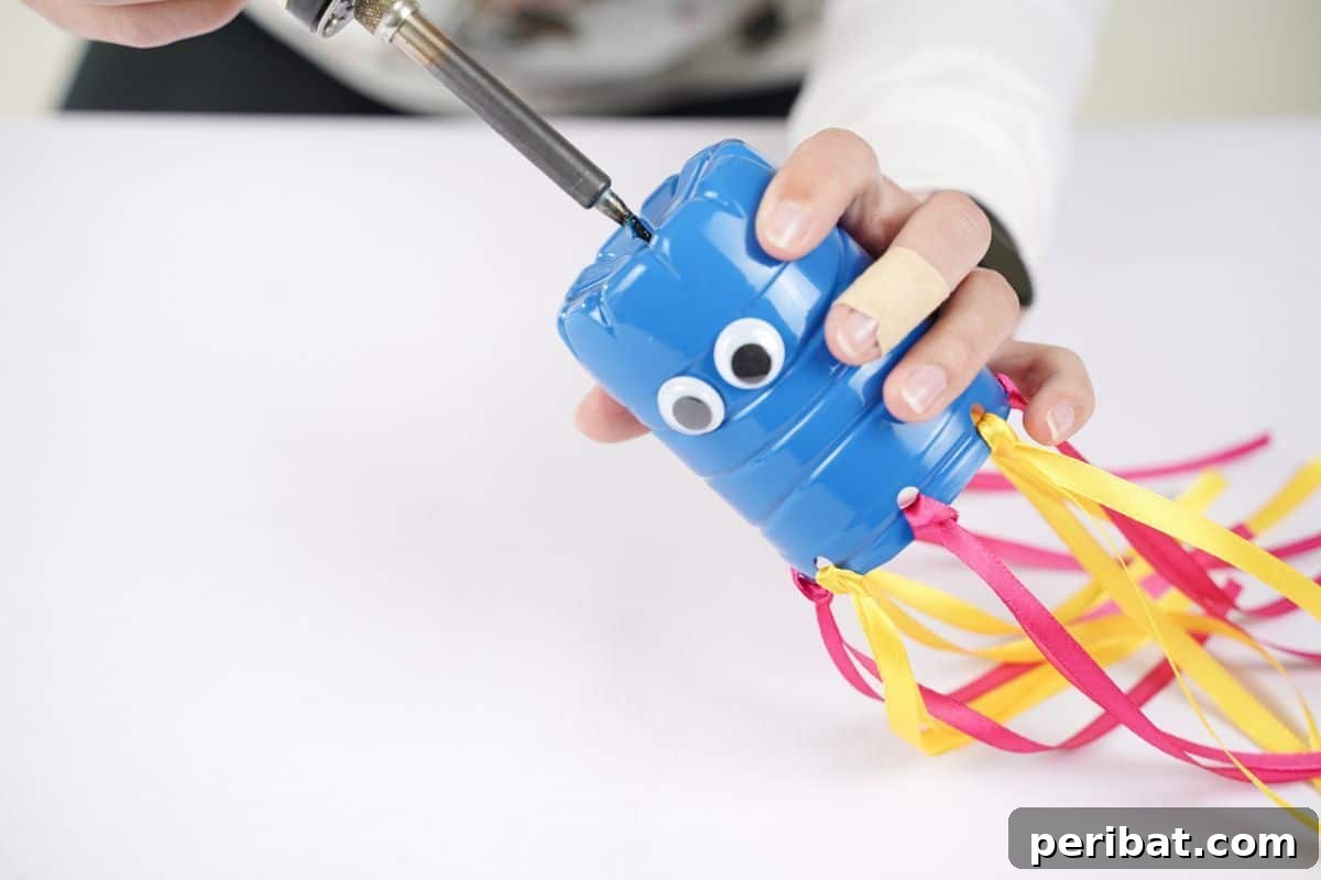 Vibrant Upcycled Bottle Wind Streamer 13 Soldering gun held above a blue plastic bottle to make a hole