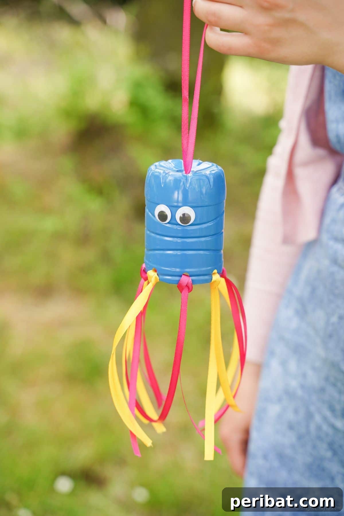 Vibrant Upcycled Bottle Wind Streamer 19 Plastic bottle windsock hanging from a woman's hand, showcasing its design