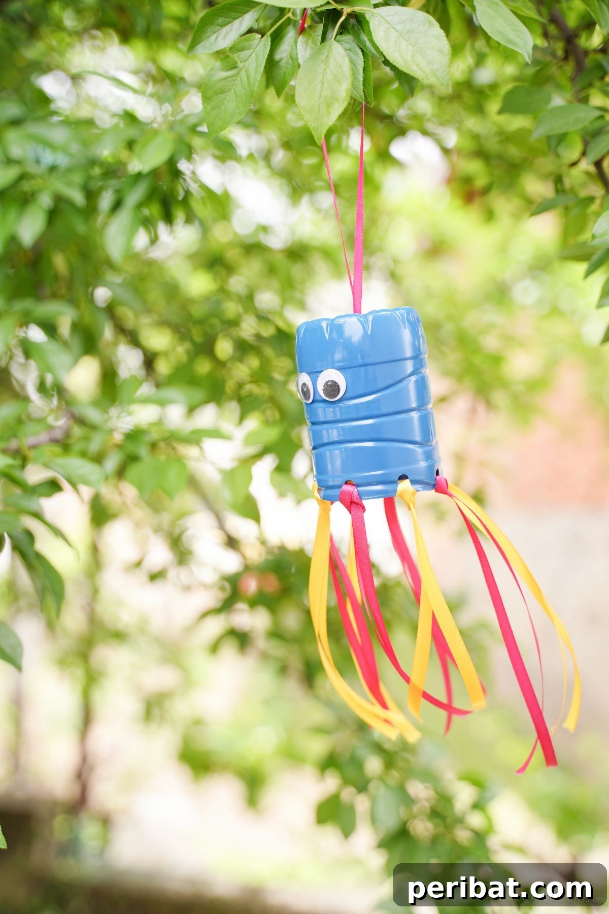 Vibrant Upcycled Bottle Wind Streamer 20 Windsock with blue top and colorful ribbons moving gently in a tree