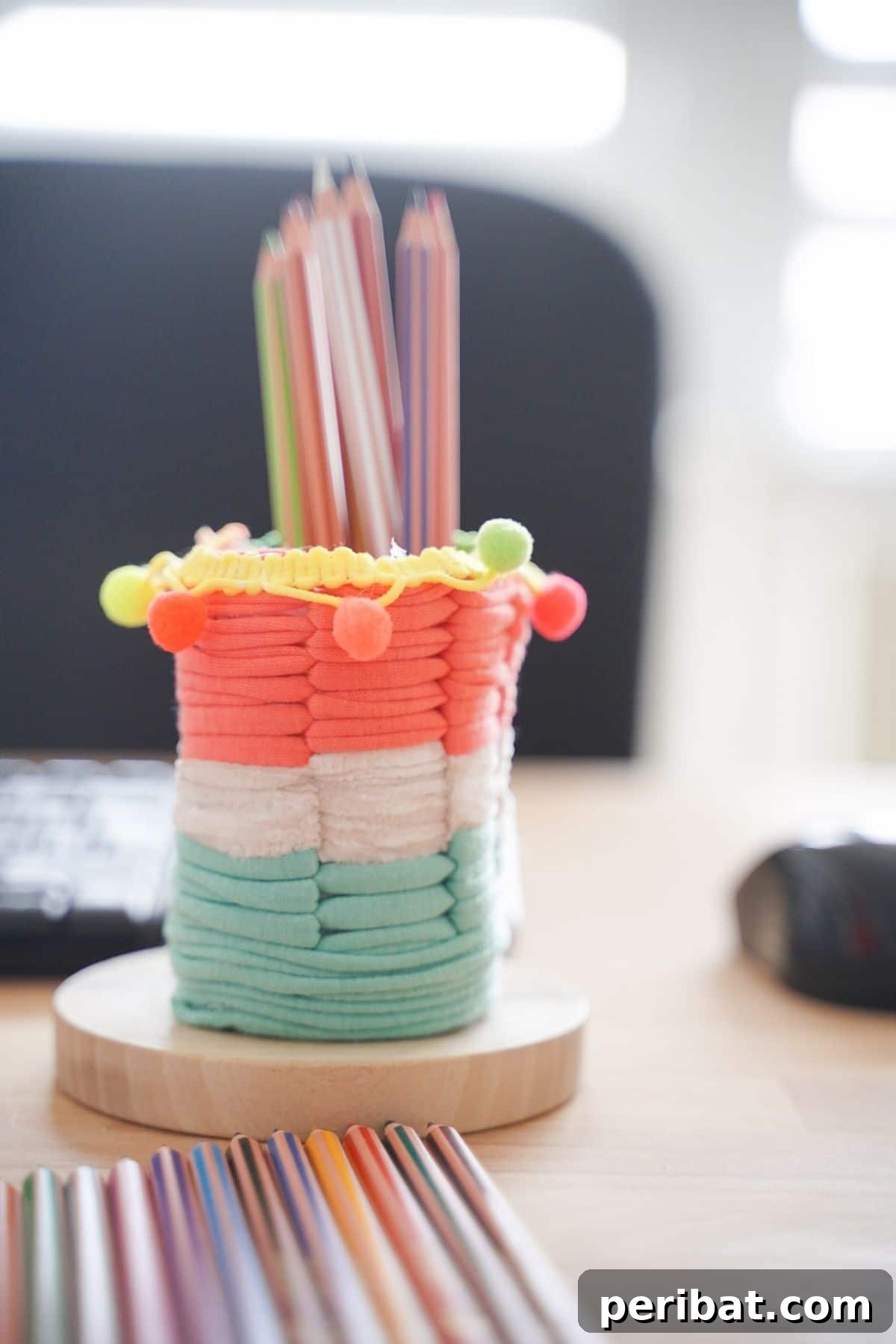 Upcycled Plastic Bottle Desk Organizer 2 Chic DIY pencil holder made from a plastic bottle, adorned with pink, white, and green yarn, sitting elegantly on a desk.