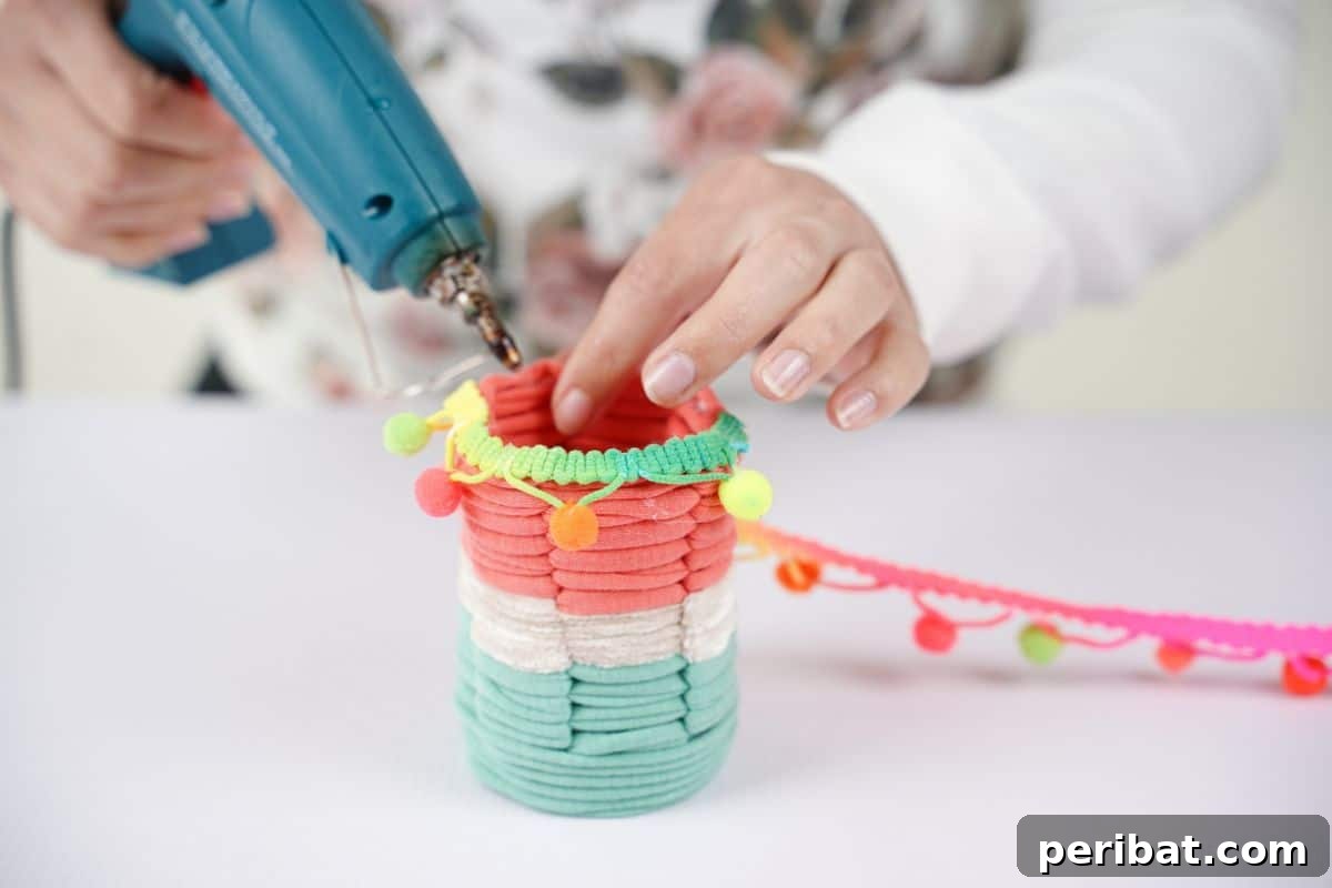 Upcycled Plastic Bottle Desk Organizer 14 A hot glue gun is used to carefully attach ribbon around the top edge of the woven pencil cup, adding a neat finish.