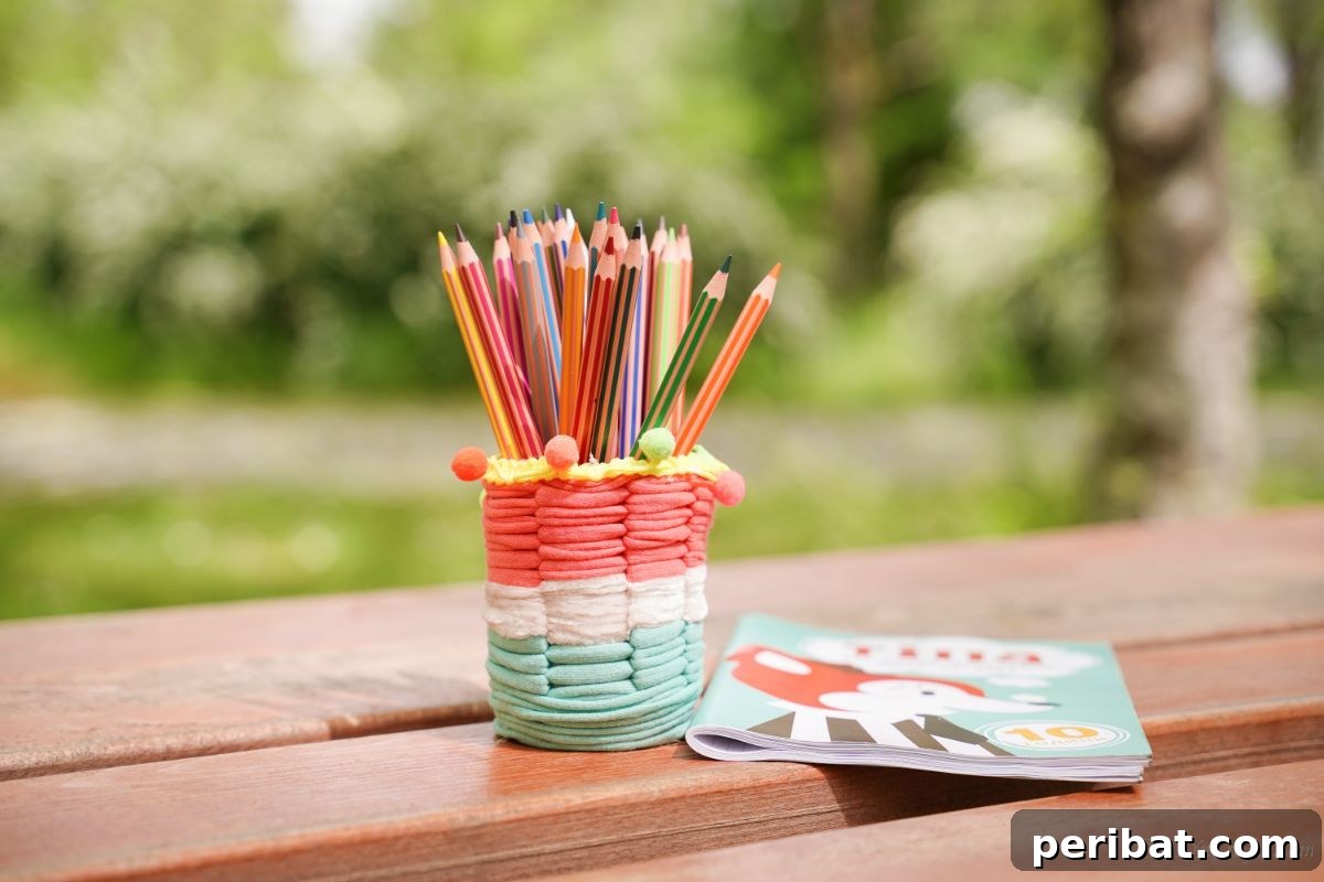 Upcycled Plastic Bottle Desk Organizer 15 A brightly striped pencil cup, crafted from yarn-covered plastic, stands on a charming picnic table next to a coloring book, inviting creativity.
