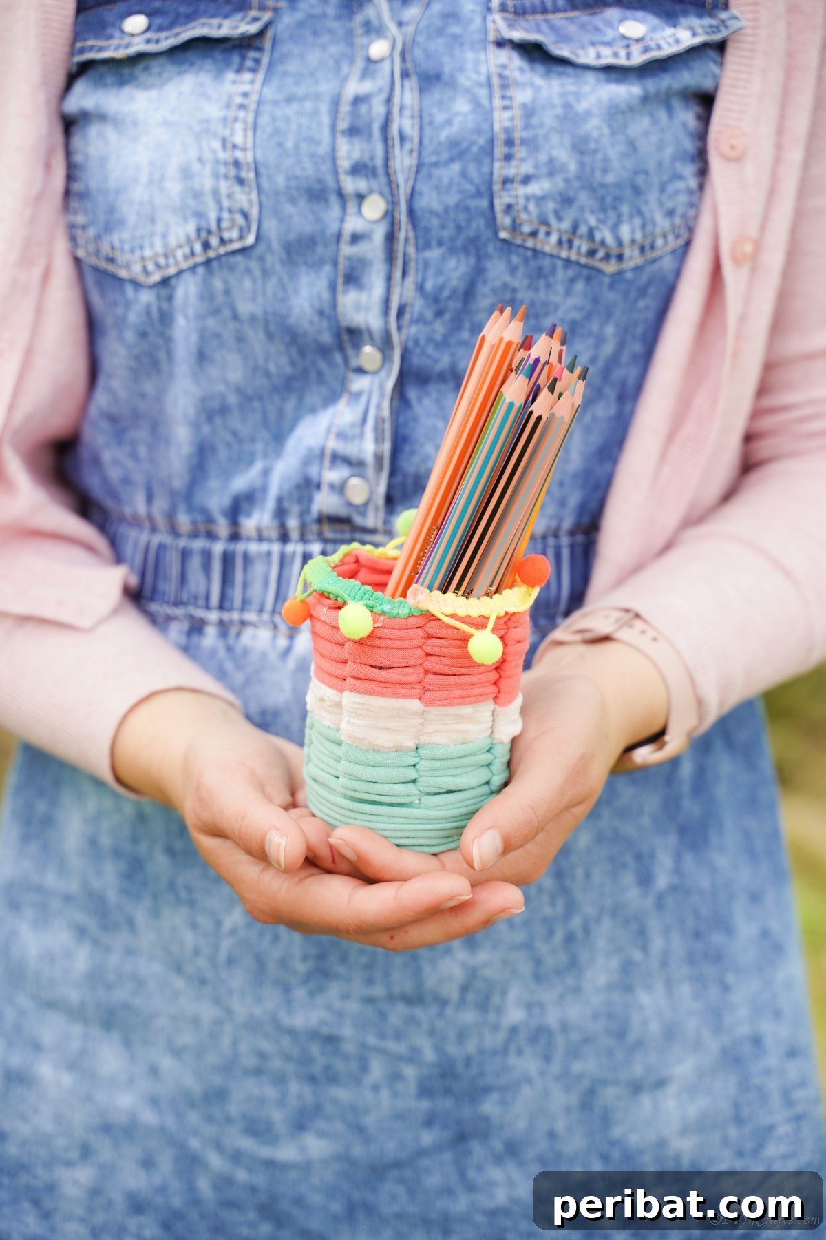 Upcycled Plastic Bottle Desk Organizer 5 A person in a denim jumper holding the finished DIY pencil holder, showcasing its practical size and appealing design.
