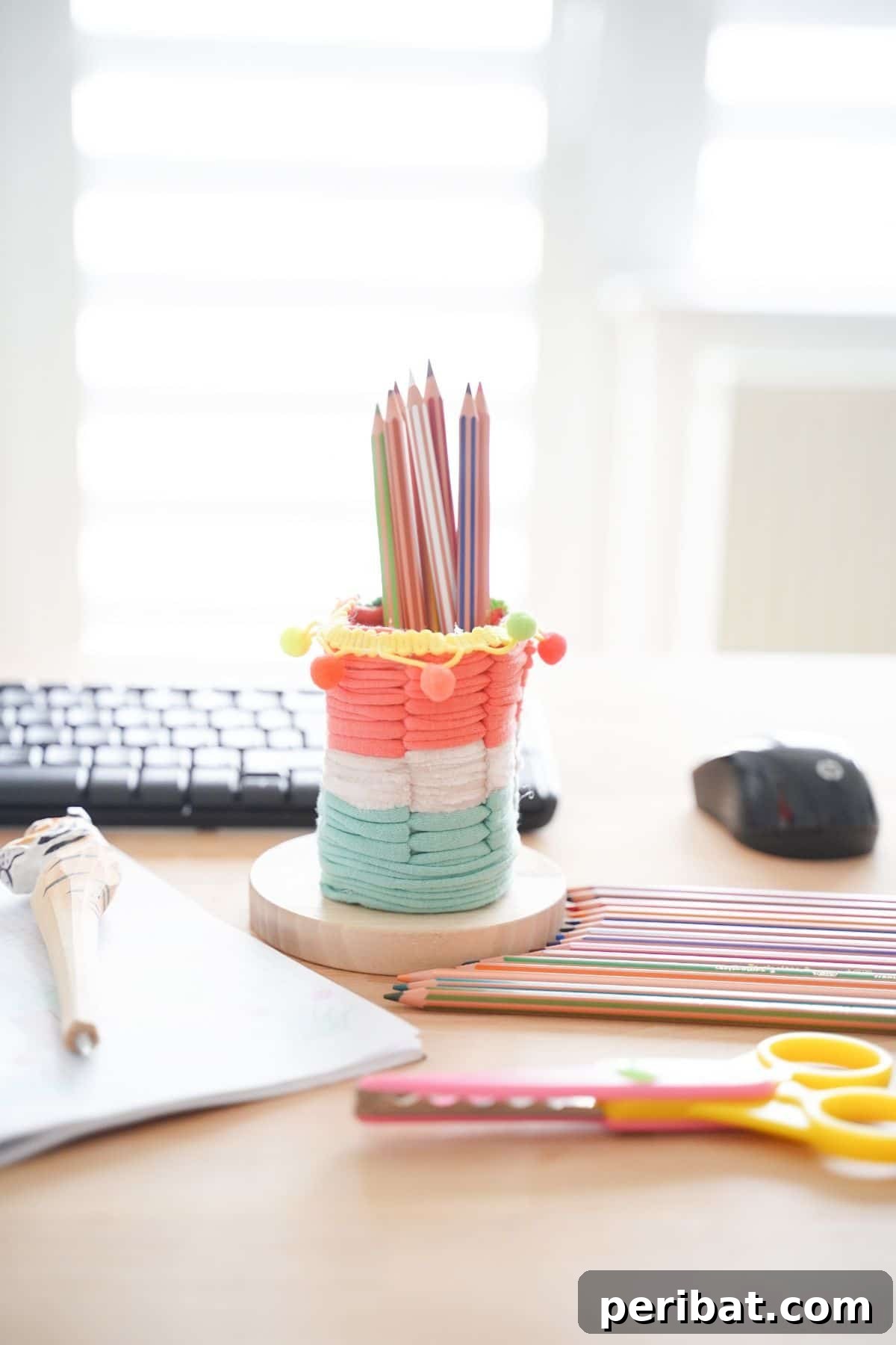 Upcycled Plastic Bottle Desk Organizer 6 Completed DIY pencil holder, adorned with colorful yarn and filled with colored pencils, placed on a rustic round wood piece.