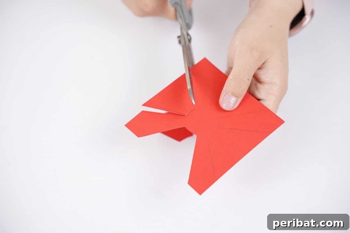 Gray scissors being used to precisely cut out the red paper propeller shape from the cardstock.