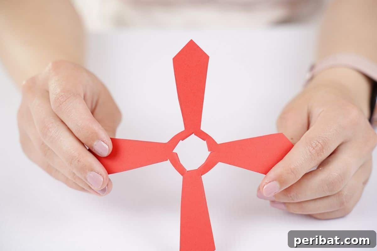 A hand holding the red paper propeller, showcasing the carefully cut slits in its center for attachment.