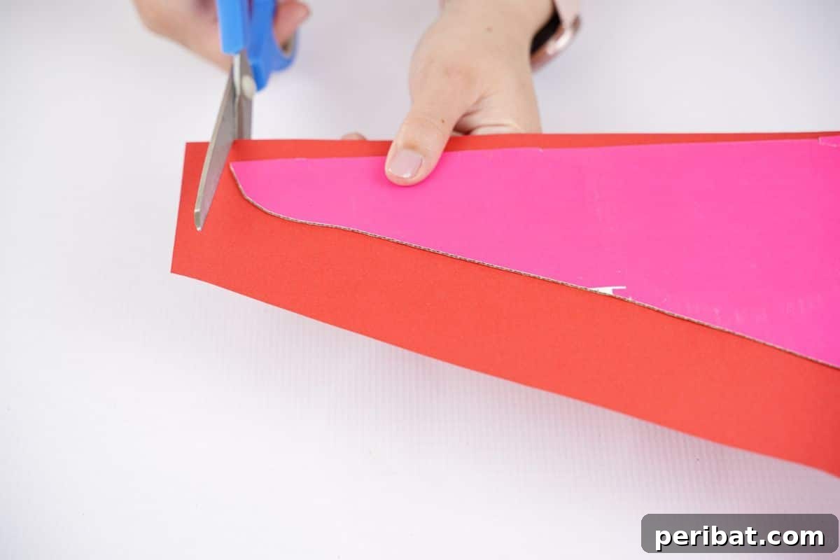 A hand carefully cutting red paper to fit over a cardboard wing, preparing it for assembly.