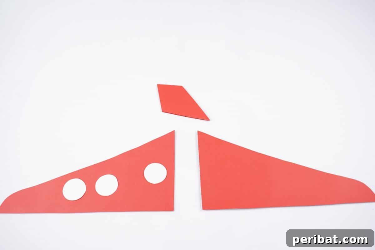 Two red wings and a red rudder resting on a white table, alongside three white paper dots destined to be airplane windows.
