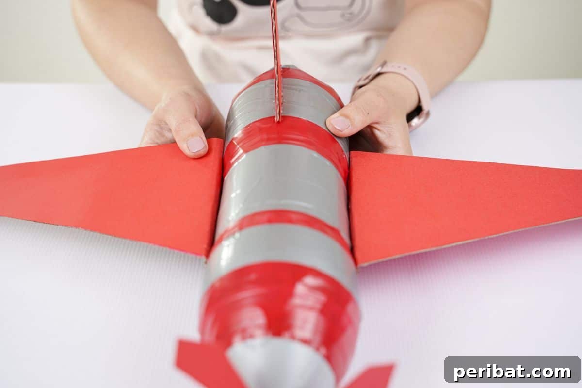 A hand holding a red wing to the side of the bottle plane, demonstrating the correct placement and attachment.