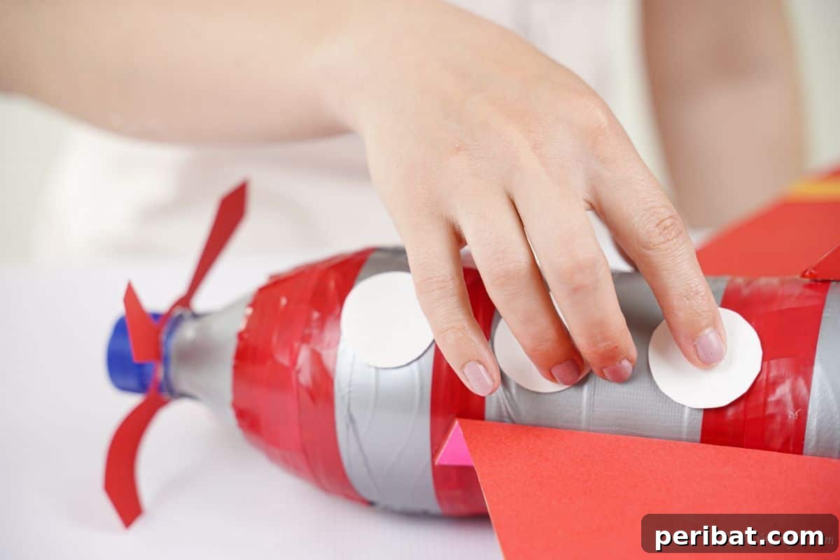White circles being glued onto the side of the plastic bottle airplane to create charming windows.
