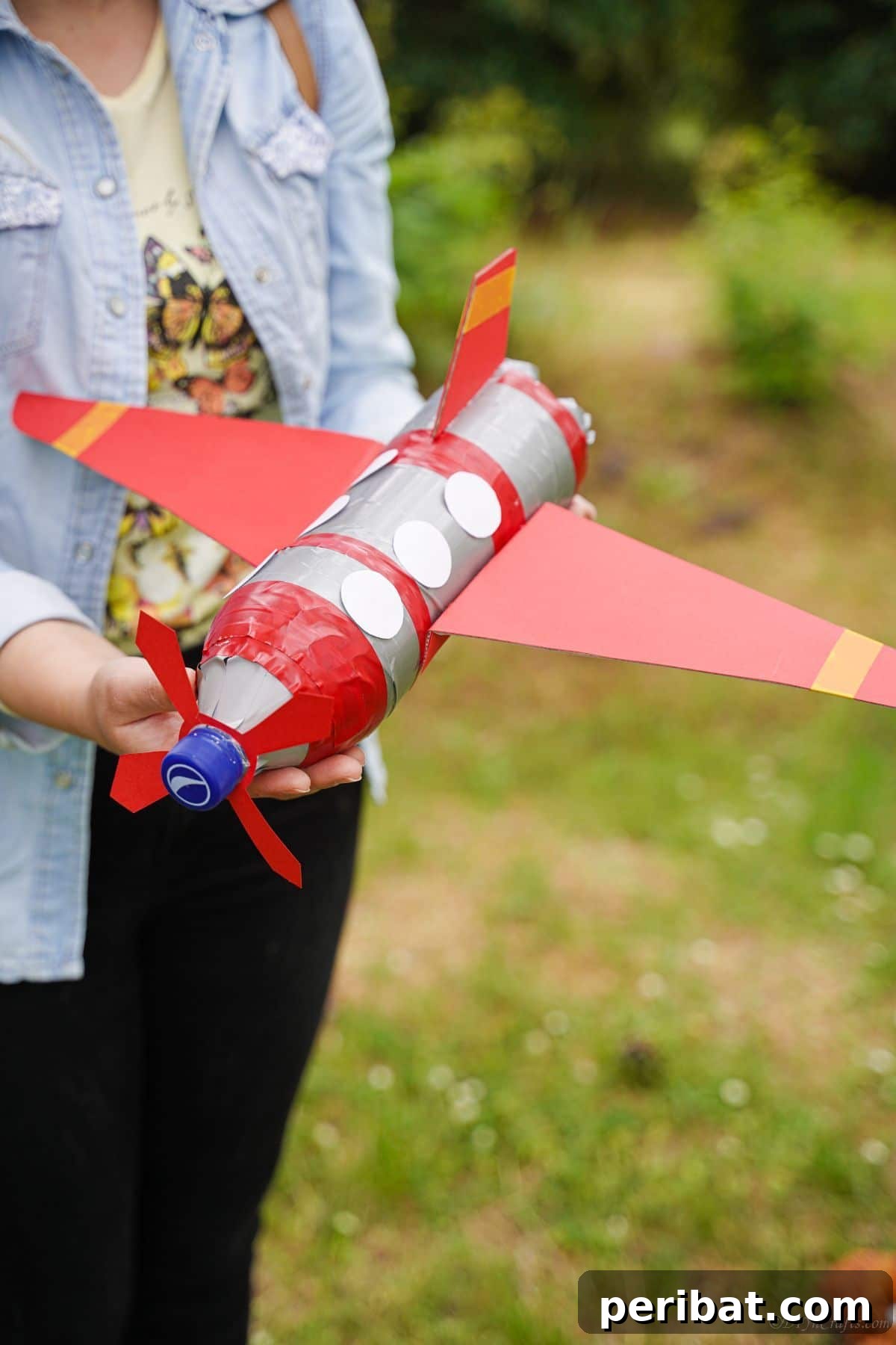 Upcycle Bottles Into Fun Toy Airplanes 4 A woman's hands gently hold a finished red and silver plastic bottle airplane, showcasing the craft.