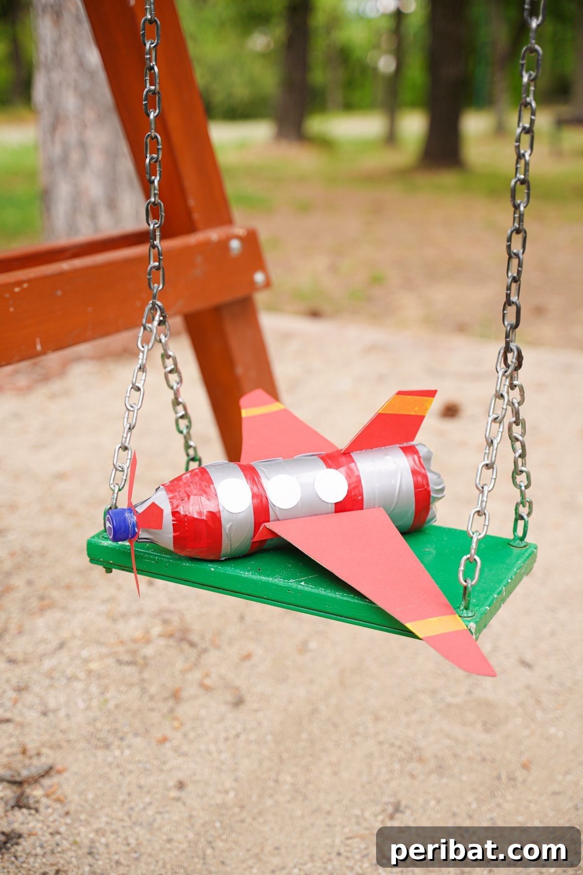 Upcycle Bottles Into Fun Toy Airplanes 23 A red and silver plastic bottle airplane rests charmingly on a swingset, ready for play.
