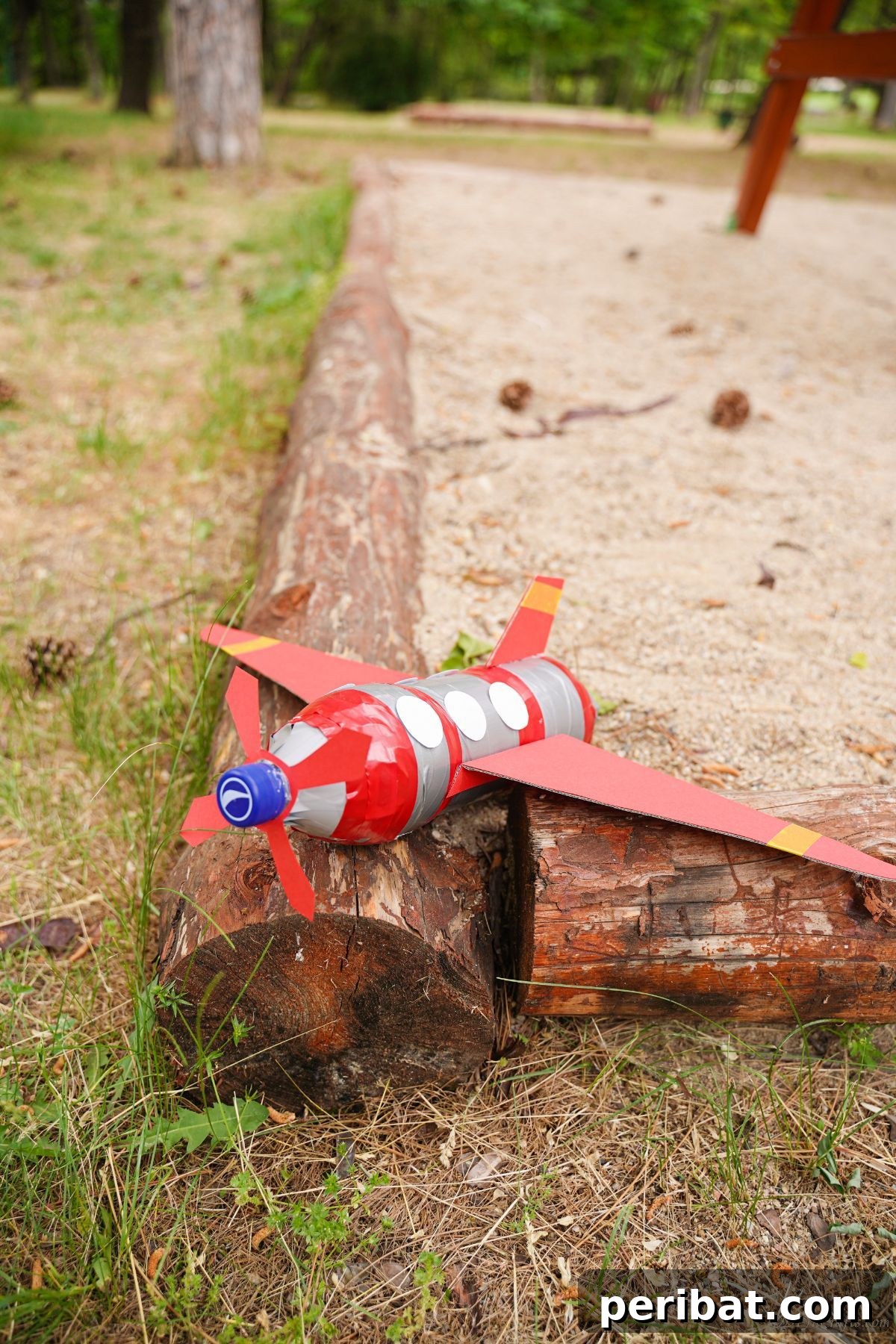 Upcycle Bottles Into Fun Toy Airplanes 24 A beautifully crafted red and silver plastic bottle airplane sits on the wood edging of a playground sandbox.