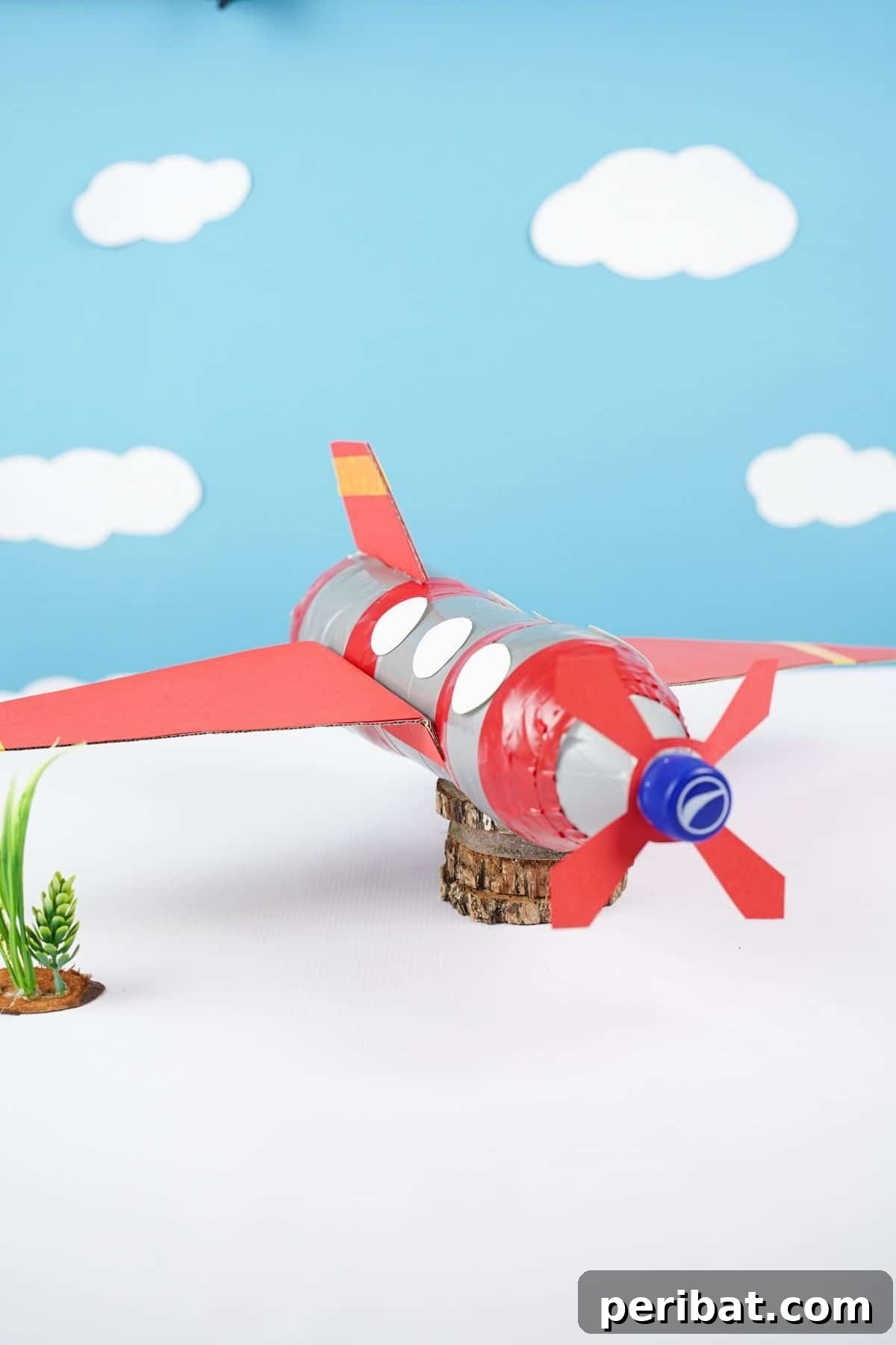 Upcycle Bottles Into Fun Toy Airplanes 6 A vibrant blue background with soft white clouds highlights a red and silver plastic bottle airplane toy, symbolizing flight.