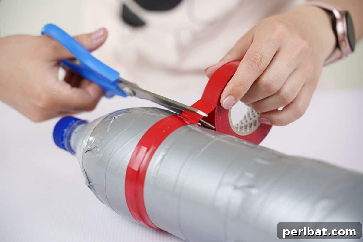 Hands wrapping red washi tape around bottle to create decorative stripes for the airplane body.