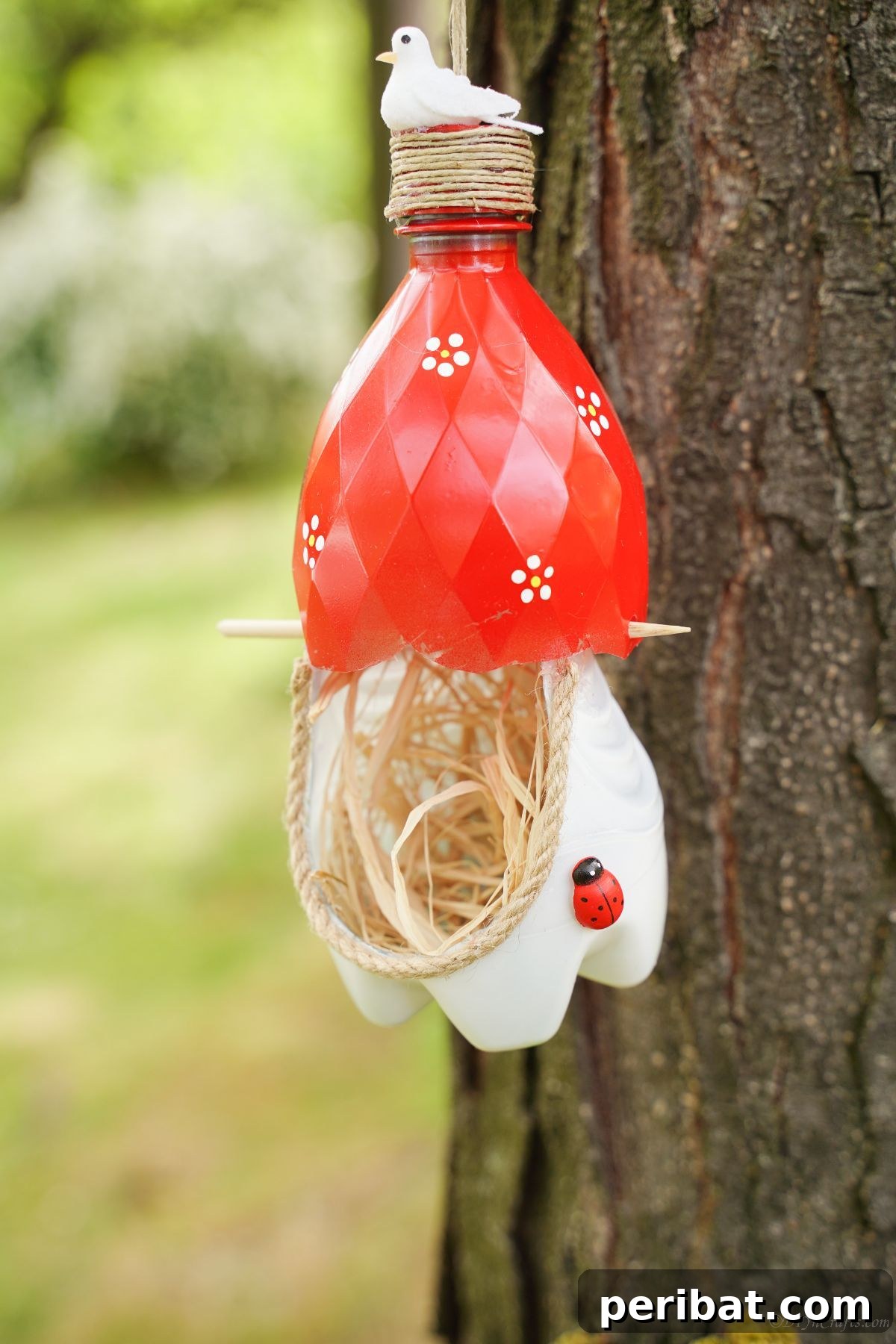 Upcycled Bottle Birdhouse 2 Close-up picture of a white and red plastic bottle bird nest hanging on a tree branch, showcasing intricate details