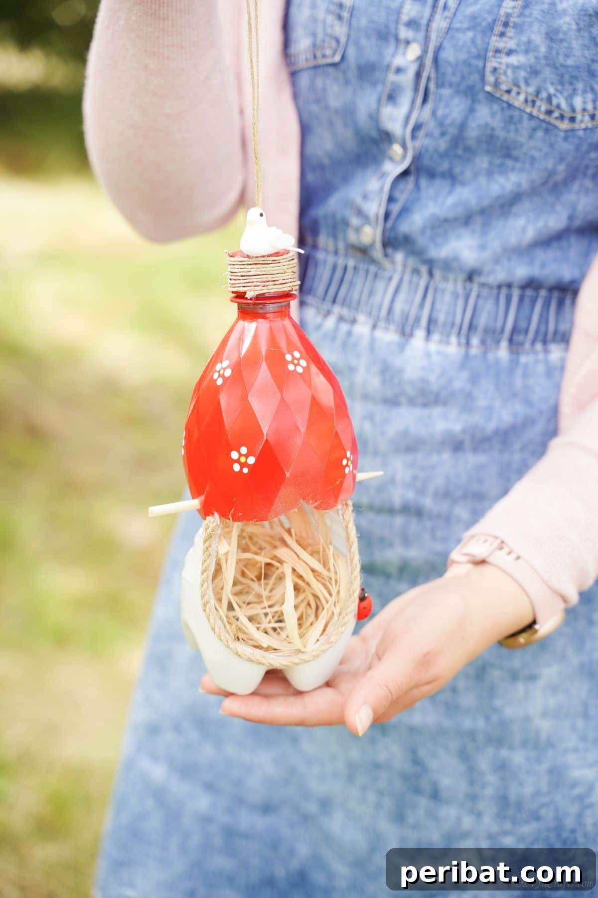 Upcycled Bottle Birdhouse 31 Woman holding a beautifully crafted red and white bird nest made from a plastic bottle, proudly presenting her DIY project