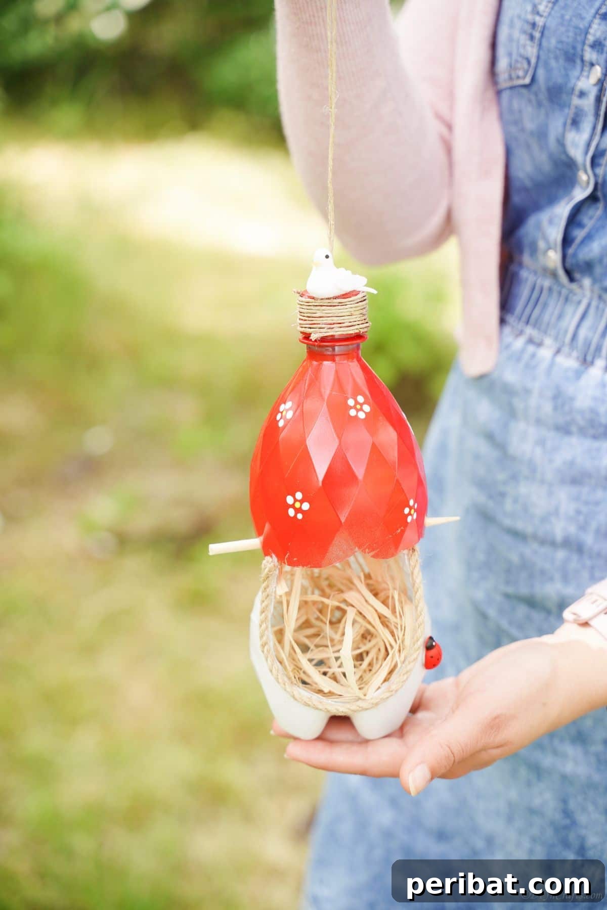 Upcycled Bottle Birdhouse 18 A woman gently holding a red and white bottle nest, ready to place it for birds