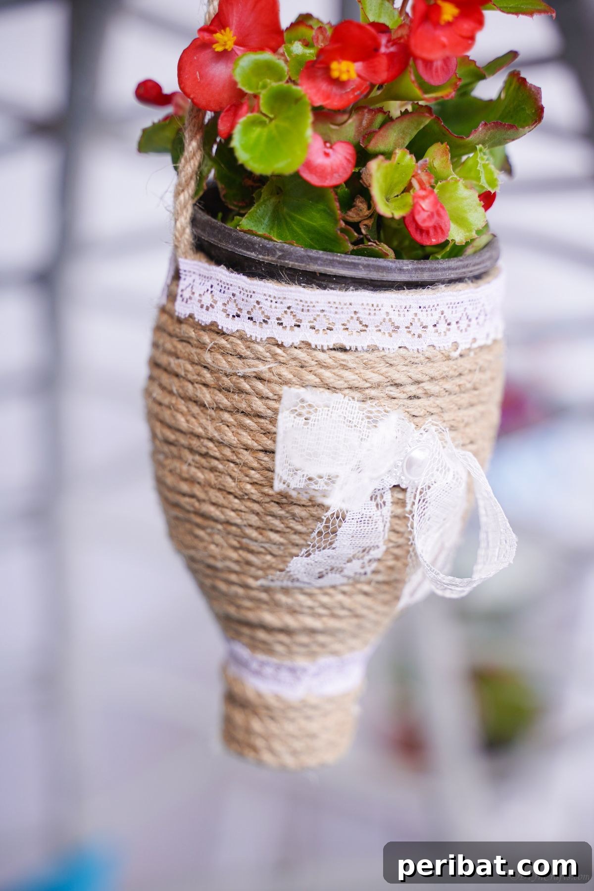 DIY Rustik İp Sarılı Şişe Bahçe Planterları 2 Close-up image of a beautifully crafted twine-wrapped bottle planter showcasing vibrant red flowers, perfect for rustic decor.