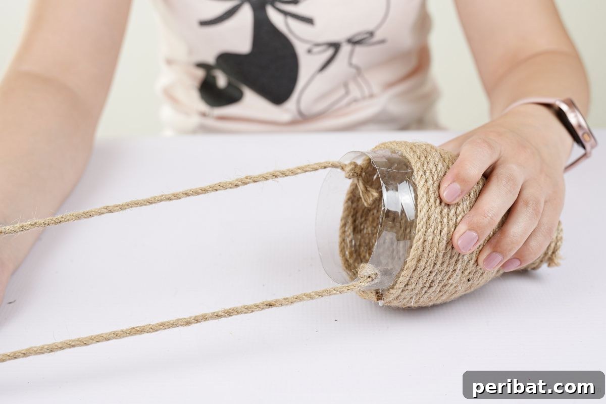 DIY Rustik İp Sarılı Şişe Bahçe Planterları 12 A hand holds a finished twine loop above the planter, demonstrating the hanging mechanism for the DIY project.