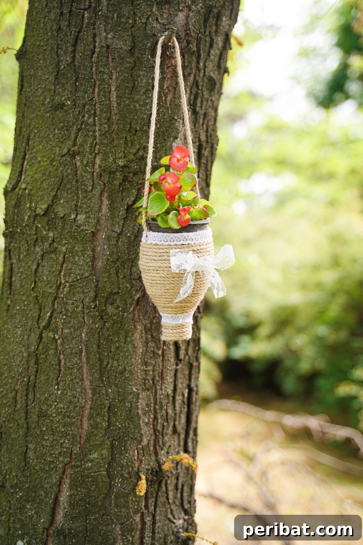 DIY Rustik İp Sarılı Şişe Bahçe Planterları 16 A completed twine-wrapped bottle planter gracefully hanging on a tree branch, adorned with vibrant flowers, showcasing its outdoor appeal.