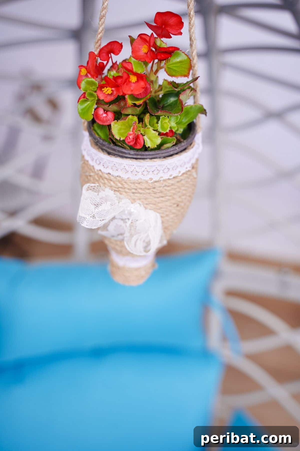 DIY Rustik İp Sarılı Şişe Bahçe Planterları 17 Flowers blooming in a rustic twine planter, elegantly hanging above a white wicker chair with a soft blue cushion.