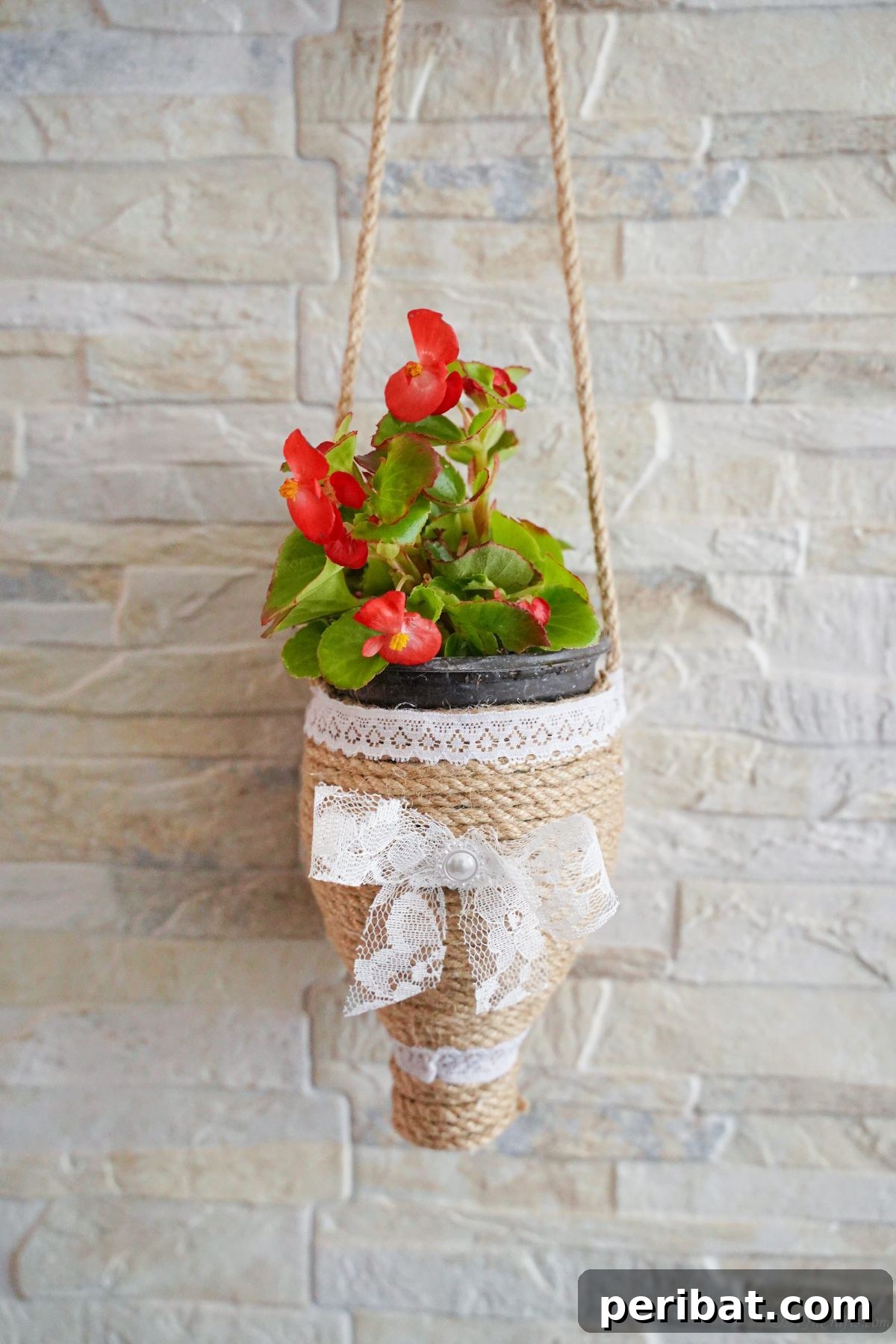 DIY Rustik İp Sarılı Şişe Bahçe Planterları 18 A beautifully crafted upcycled water bottle planter hanging gracefully on a cream brick wall, showcasing its rustic charm.