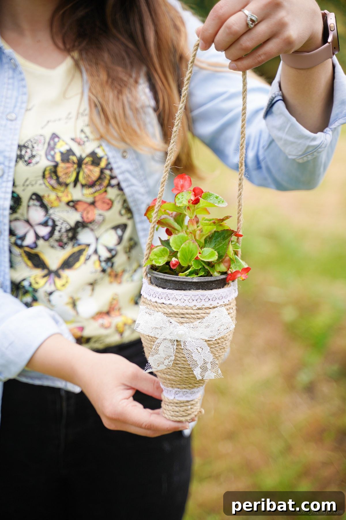 DIY Rustik İp Sarılı Şişe Bahçe Planterları 4 Woman holding a twine planter filled with vibrant red flowers, showcasing the completed DIY project in hand.