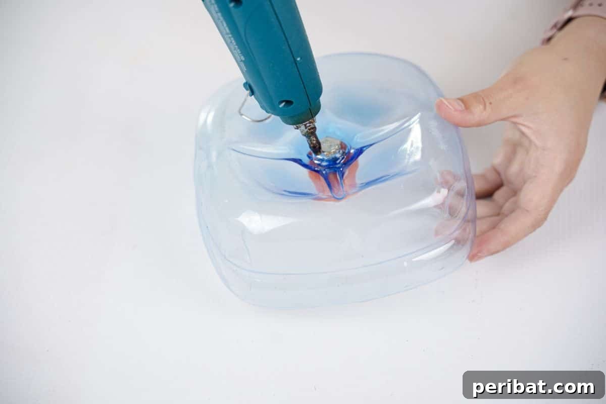 Recycled Bottle Bird Retreat 11 hot glue being applied to the bottom of the plastic bottle bird feeder base to seal the connections