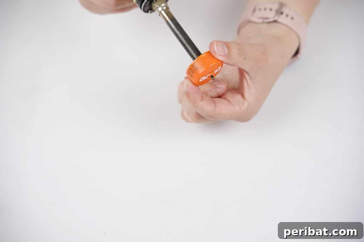 Recycled Bottle Bird Retreat 9 a soldering iron meticulously drilling a hole into the center of an orange plastic bottle cap