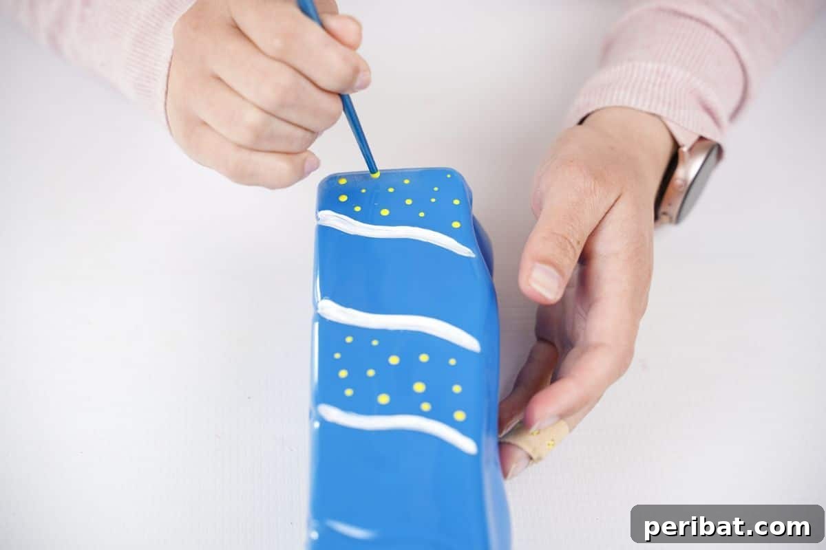 Craft Upcycled Bottle Characters for a DIY Bowling Game 13 A hand carefully painting white polka dots onto a blue painted plastic bottle, creating a playful clothing pattern.