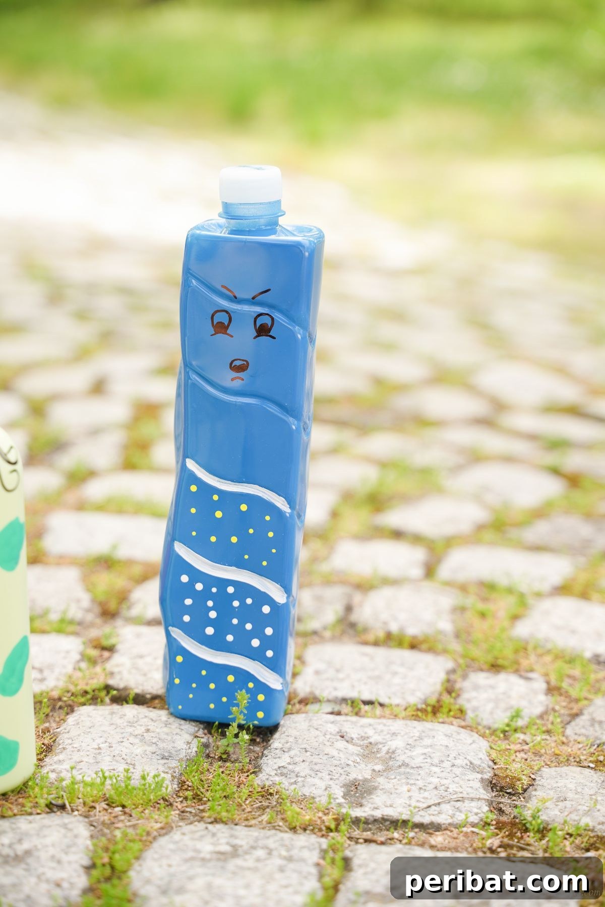 Craft Upcycled Bottle Characters for a DIY Bowling Game 18 A blue and white painted plastic bottle character standing on a cobblestone walkway, ready for imaginative play.