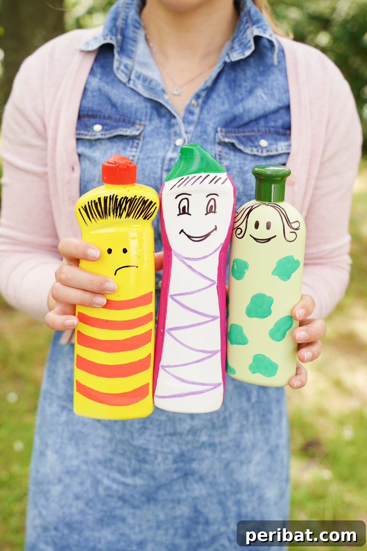 Craft Upcycled Bottle Characters for a DIY Bowling Game 6 A woman's hands gently holding three painted plastic bottle characters – yellow, white, and green – showcasing their cheerful designs.