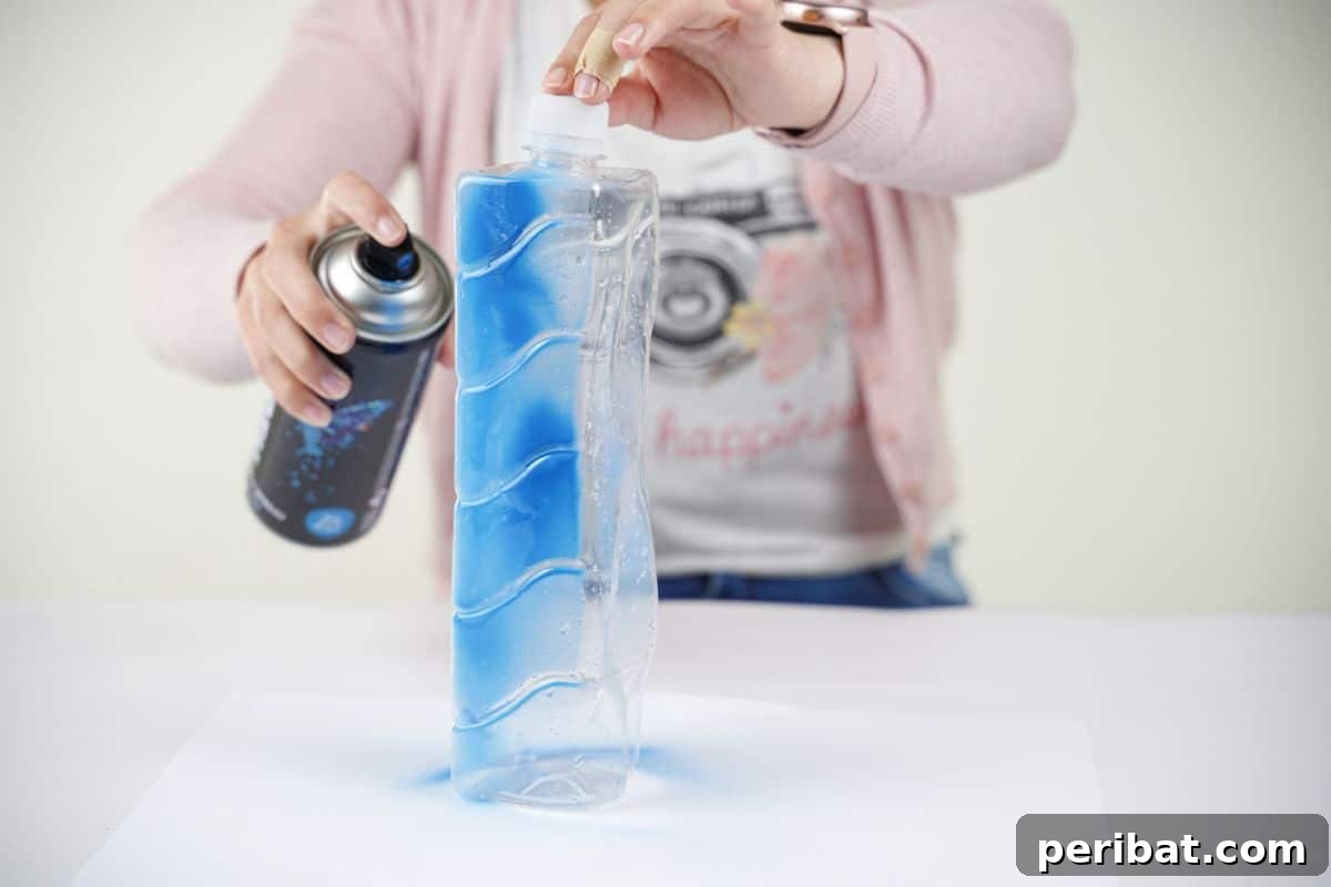 Craft Upcycled Bottle Characters for a DIY Bowling Game 9 A person in a pink sweater carefully applies blue spray paint to a clear plastic bottle, preparing it for decoration.