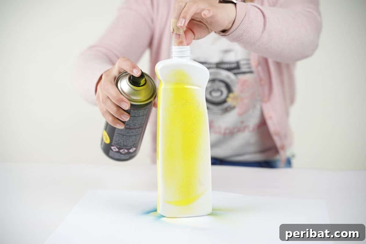 Craft Upcycled Bottle Characters for a DIY Bowling Game 10 A hand holding a white bottle as it is being sprayed with vibrant yellow paint, demonstrating the base coat application.