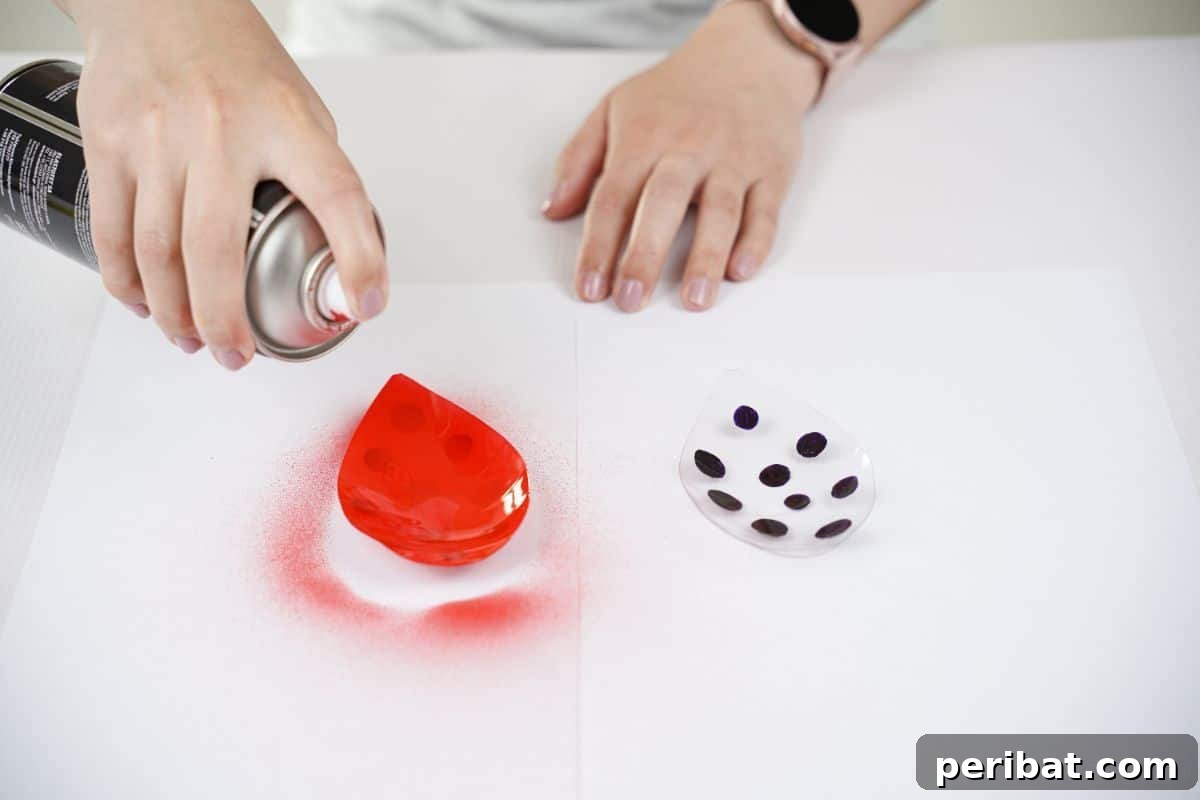 Charming Ladybug Garden Decor from Upcycled Bottles 14 A hand delicately spraying the back of a plastic wing piece with red paint, creating the vibrant color for the ladybug's outer shell.