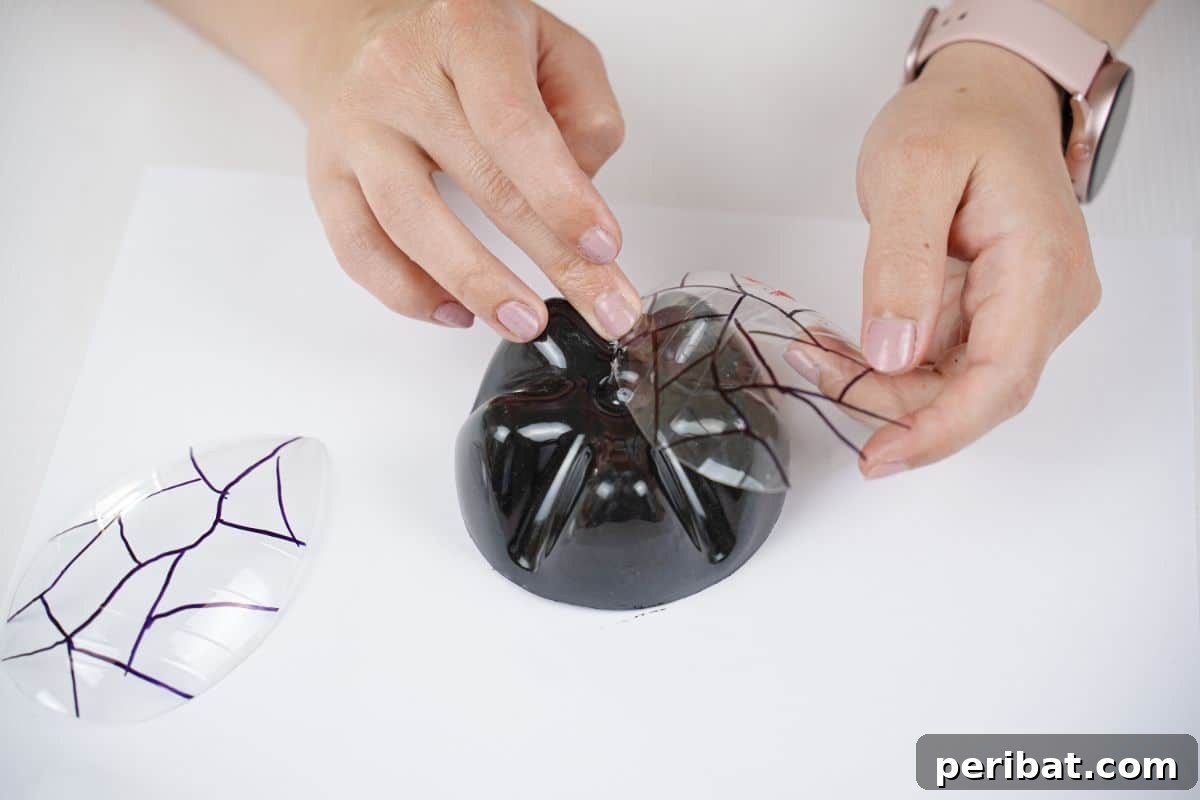 Charming Ladybug Garden Decor from Upcycled Bottles 16 A hand applying hot glue to a clear wing shape before attaching it to the bottle base, demonstrating the assembly process.