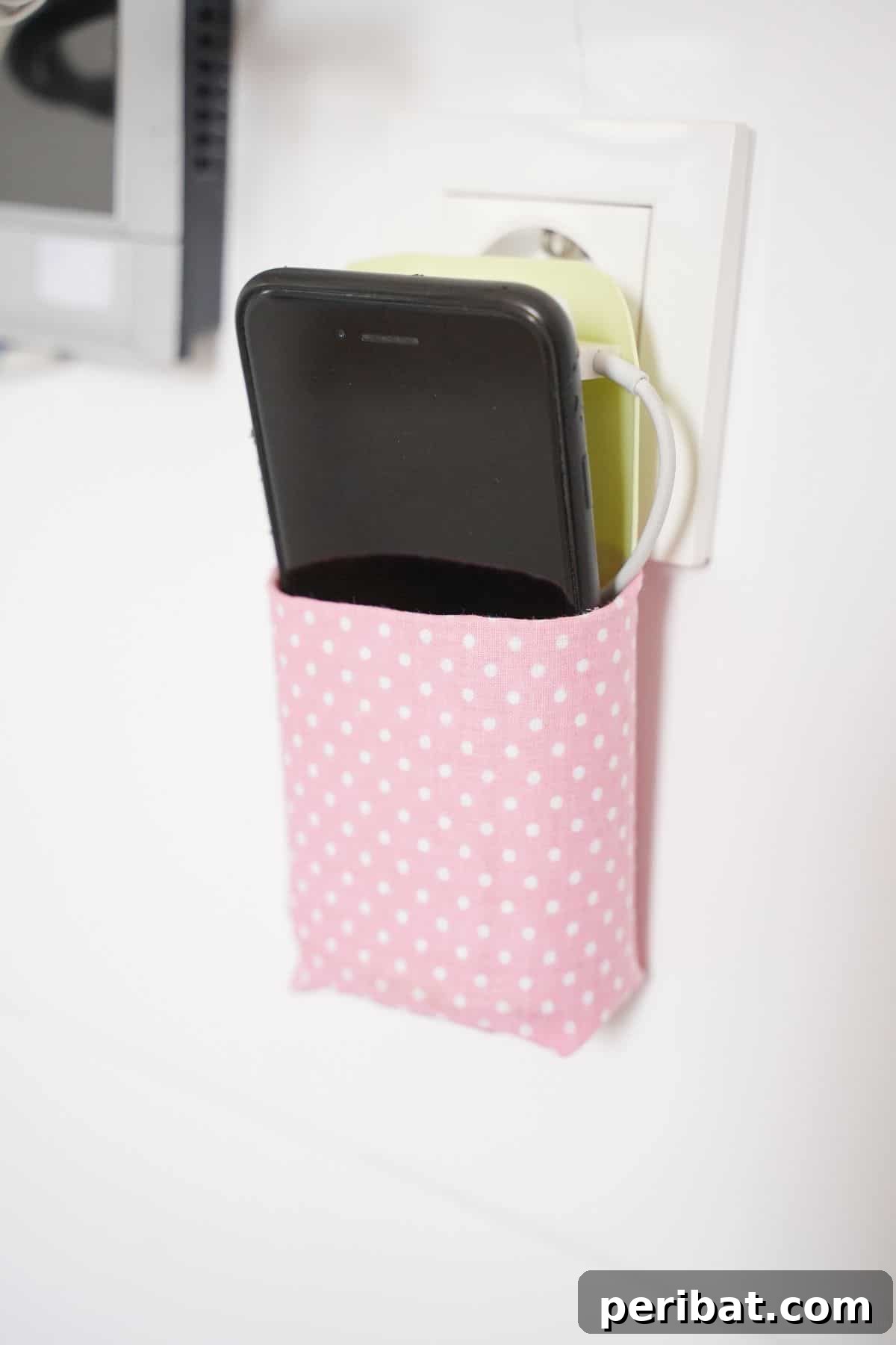 white and pink holder for cellphone hanging on white outlet