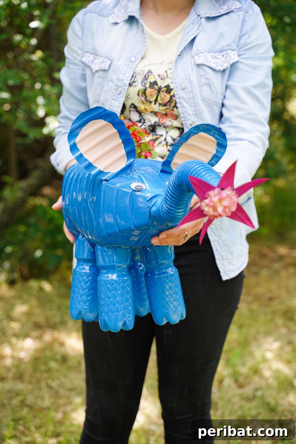 Upcycled Bottles Blossom into Adorable Elephant Planters 6 woman in black pants holding bright blue elephant planter