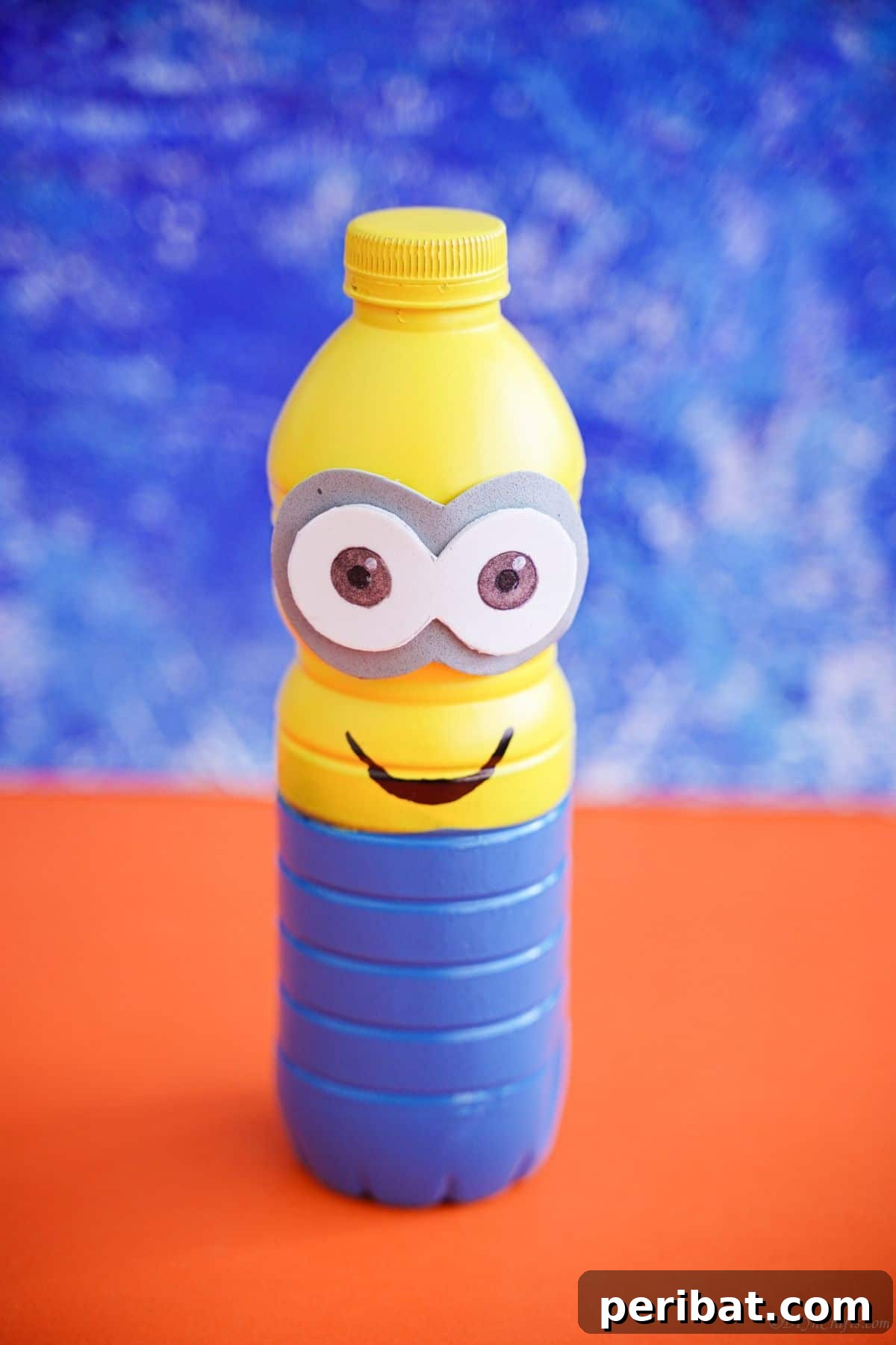 Upcycled Bottle Minion Creations 2 Adorable Minion bottle craft on a vibrant orange table, set against a cheerful blue background, ready for display.