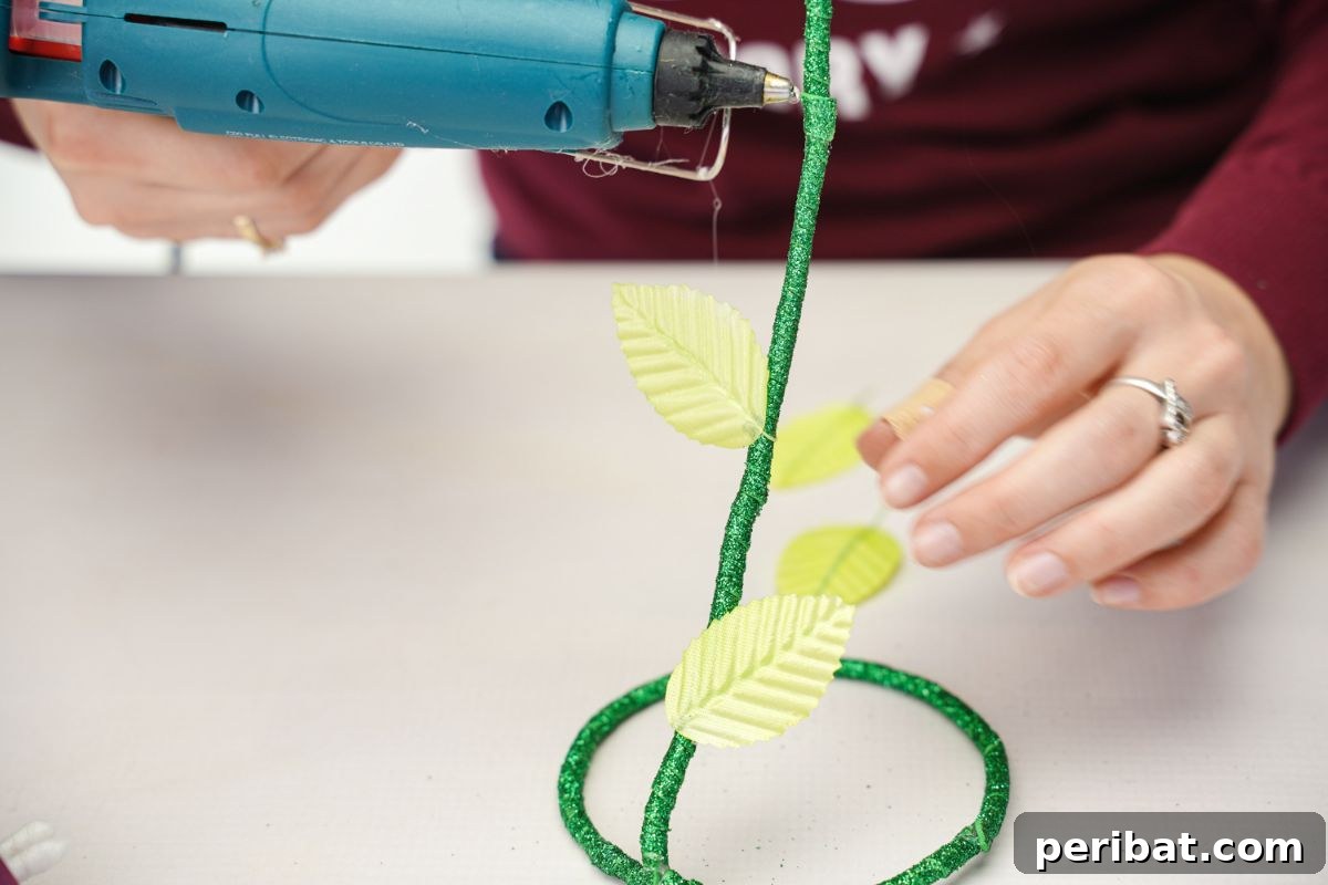 Upcycled Plastic Bottle Blossoms 13 Hot glue gun attaching fake leaves to a green glitter foam paper stem